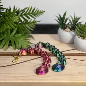 May include: Two articulated keychains featuring a series of connected, geometric, multi-faceted segments. One keychain transitions from pink to orange, while the other shifts from green to blue. Each includes a gold-toned metal lobster clasp.