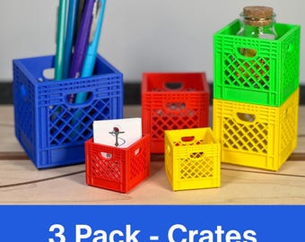 May include: A selection of small, brightly coloured crates in blue, red, green, and yellow. A blue crate contains pens, while others are empty or hold small objects. The text "3 Pack - Crates" is visible at the bottom.
