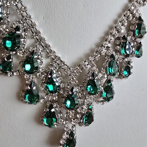May include: A silver-toned necklace with a cascading design. The necklace features numerous clear, round-cut crystals and teardrop-shaped, emerald-green gemstones. The gemstones are set in a silver-toned metal, creating a sparkling and elegant accessory.