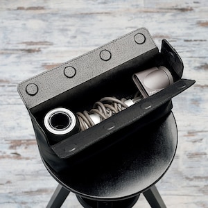 May include: A black leather carrying case with a zippered opening, containing a gray hair dryer, a black cylindrical object, and a coiled gray cord.