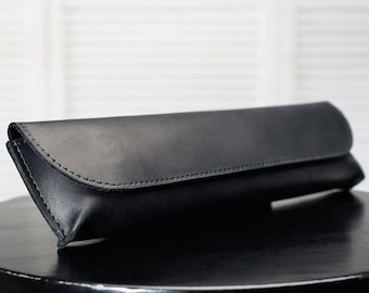 Puede incluir: Un bolso de mano de cuero negro con cierre de solapa y detalle de costura.