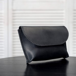 Puede incluir: Un bolso de mano de cuero negro con cierre de solapa. El bolso est&aacute; sobre una mesa negra.