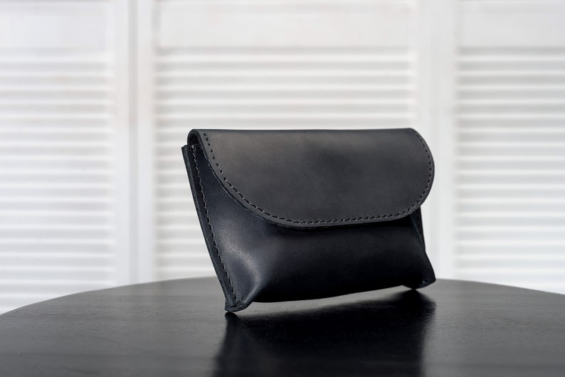 Puede incluir: Un bolso de mano de cuero negro con cierre de solapa. El bolso est&aacute; sobre una mesa negra.