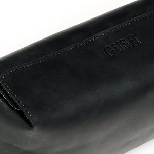 Puede incluir: Bolsa de cremallera de cuero negro con la palabra "GUSH" grabada en la parte delantera.