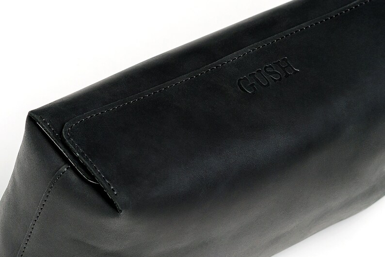 Puede incluir: Bolsa de cremallera de cuero negro con la palabra "GUSH" grabada en la parte delantera.