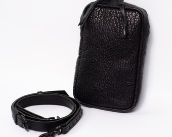 Puede incluir: Un bolso bandolera de cuero negro con acabado texturizado y correa desmontable.