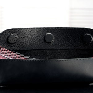 Puede incluir: Una funda de cuero negro con tres broches, abierta para revelar dos peines rojos y transparentes en el interior.