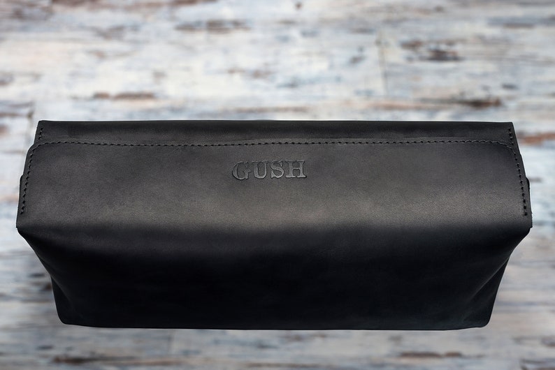 Puede incluir: Bolsa de cuero negro con la palabra "GUSH" grabada en la parte delantera.