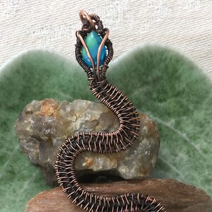 May include: A copper wire wrapped snake pendant with a blue iridescent gemstone in the head.