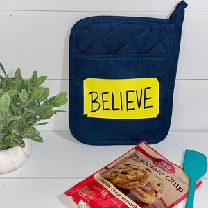 May include: A blue quilted pot holder with a yellow label that says "BELIEVE".