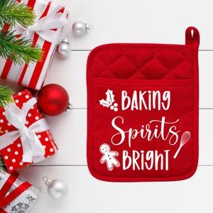 Pode incluir: Uma luva de forno acolchoada vermelha com as palavras "BAKING Spirits BRIGHT" em letras brancas. A luva tem um bolso e uma argola para pendurar. Presentes e enfeites de Natal no fundo.