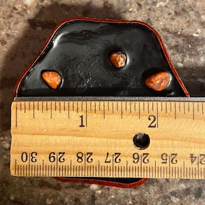 Puede incluir: Una bandeja de resina negra con tres peque&ntilde;as piedras rojas de forma irregular. La bandeja mide aproximadamente 4,4 cm de ancho y est&aacute; sobre una regla de madera.