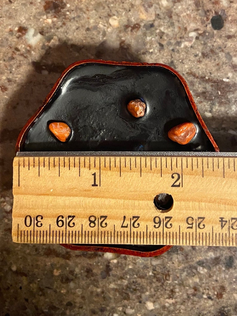 Puede incluir: Una bandeja de resina negra con tres peque&ntilde;as piedras rojas de forma irregular. La bandeja mide aproximadamente 4,4 cm de ancho y est&aacute; sobre una regla de madera.