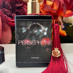 K&ouml;nnte beinhalten: Eine schwarze Parfumflasche mit goldener Kappe und rotem Quast. Die Flasche ist mit "Sacred Lore Botanicals Persephone Botanical Parfum" beschriftet.