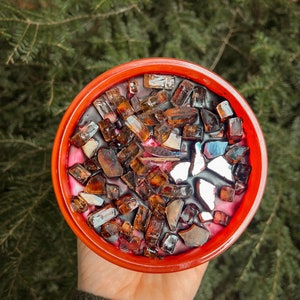 May include: A red candle jar with a black wax base and a layer of brown and silver glitter on top.