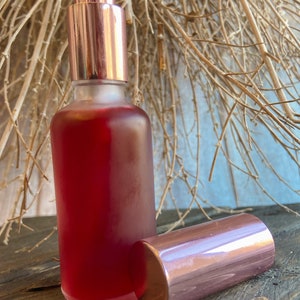 K&ouml;nnte beinhalten: Eine klare Glasflasche mit einer rosafarbenen Fl&uuml;ssigkeit und einem ros&eacute;goldenen Spr&uuml;hkopf und Verschluss. Die Flasche steht auf einer Holzoberfl&auml;che.