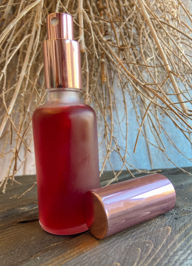 K&ouml;nnte beinhalten: Eine klare Glasflasche mit einer rosafarbenen Fl&uuml;ssigkeit und einem ros&eacute;goldenen Spr&uuml;hkopf und Verschluss. Die Flasche steht auf einer Holzoberfl&auml;che.