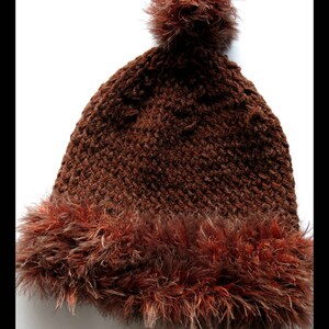 Peut inclure: Un bonnet en tricot marron avec un pompon en fausse fourrure marron et une bordure en fausse fourrure marron. Le bonnet est crocheté et présente un motif texturé.