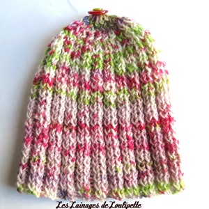 Peut inclure: Un bonnet tricoté rose, vert et blanc avec un bouton rouge sur le dessus. Le bonnet est réalisé avec un point texturé et a une coupe ample.