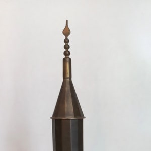 May include: A tall, brass, decorative object shaped like a tower with a pointed top. The object has a cylindrical base and a decorative top.