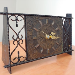 May include: A vintage clock with a dark brown face and gold hands, set within a black metal frame with decorative scrollwork.