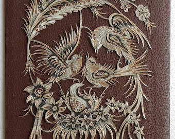May include: A brown leather background with a silver and gold embossed design of three birds and flowers.