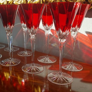 Könnte beinhalten: Ein Satz von acht roten Weingläsern mit einem klaren Kristallstiel und einer klaren Kristallbasis. Die Gläser sind in einer Reihe auf einer Holzoberfläche angeordnet.