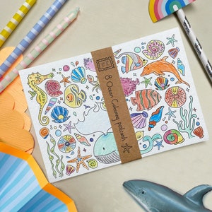 May include: A set of eight blank postcards featuring an ocean theme. The postcards are ready to be coloured with crayons, markers, or coloured pencils. The illustrations include a whale, seahorse, fish, starfish, and seashells.