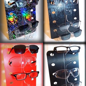 Puede incluir: Cuatro expositores diferentes para gafas, cada uno con un patrón diferente. Los expositores están hechos de acrílico transparente y tienen múltiples ranuras para sujetar las gafas. Los patrones son de fibra de carbono en blanco y negro, fibra de carbono roja, piel de cocodrilo en blanco y negro y un patrón de arcoíris.