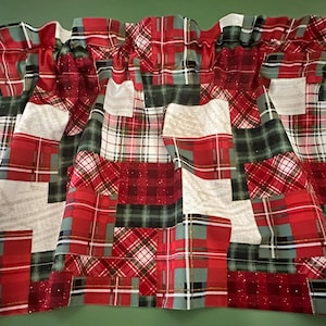 May include: A valance with a patchwork design featuring red, green, and white plaid patterns. The fabric has a mix of textures, including some with glitter accents. The valance is gathered at the top.