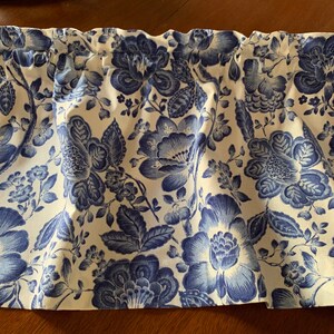 May include: A white valance with a blue floral pattern. The valance has a ruffled edge and is made of a soft, lightweight fabric.
