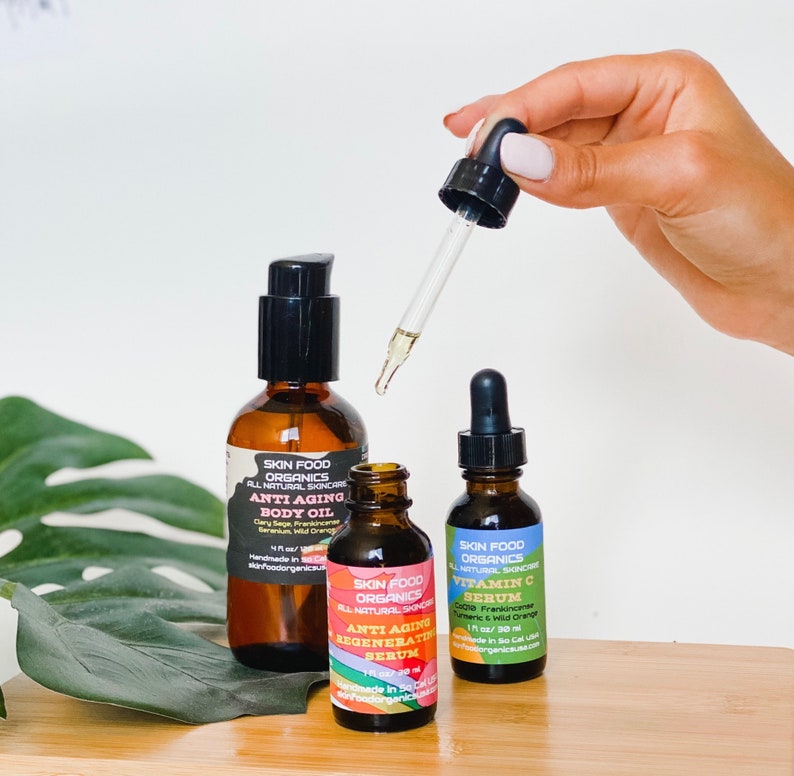 K&ouml;nnte beinhalten: Drei bernsteinfarbene Glasflaschen mit Tropfern, die Hautpflegeprodukte enthalten. Die Flaschen sind mit "Skin Food Organics" beschriftet und enthalten "Anti-Aging K&ouml;rper&ouml;l", "Anti-Aging Regenerierendes Serum" und "Vitamin C Serum".