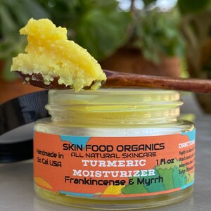 K&ouml;nnte beinhalten: Ein kleines Glas mit einer gelben Kurkuma-Feuchtigkeitscreme, aus dem mit einem Holzl&ouml;ffel eine gelbe Creme entnommen wird. Das Glas tr&auml;gt ein Etikett mit der Aufschrift "Skin Food Organics All Natural Skincare Turmeric Moisturizer Frankincense & Myrrh 1 fl oz."