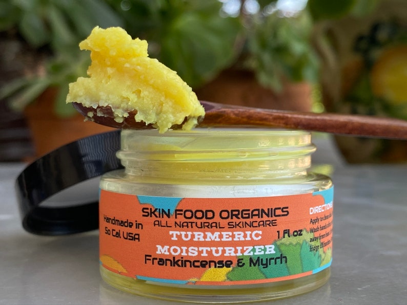 K&ouml;nnte beinhalten: Ein kleines Glas mit einer gelben Kurkuma-Feuchtigkeitscreme, aus dem mit einem Holzl&ouml;ffel eine gelbe Creme entnommen wird. Das Glas tr&auml;gt ein Etikett mit der Aufschrift "Skin Food Organics All Natural Skincare Turmeric Moisturizer Frankincense & Myrrh 1 fl oz."