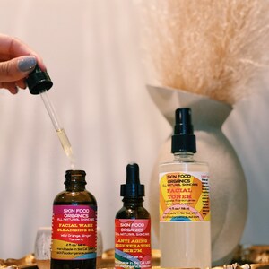 K&ouml;nnte beinhalten: Drei Glasflaschen mit Bio-Hautpflegeprodukten. Die Flaschen sind mit "Skin Food Organics" beschriftet und enthalten Gesichtswasch-Reinigungs&ouml;l, Anti-Aging-Regenerations-Serum und Gesichtswasser. Die Flaschen stehen auf einem goldenen Tablett.