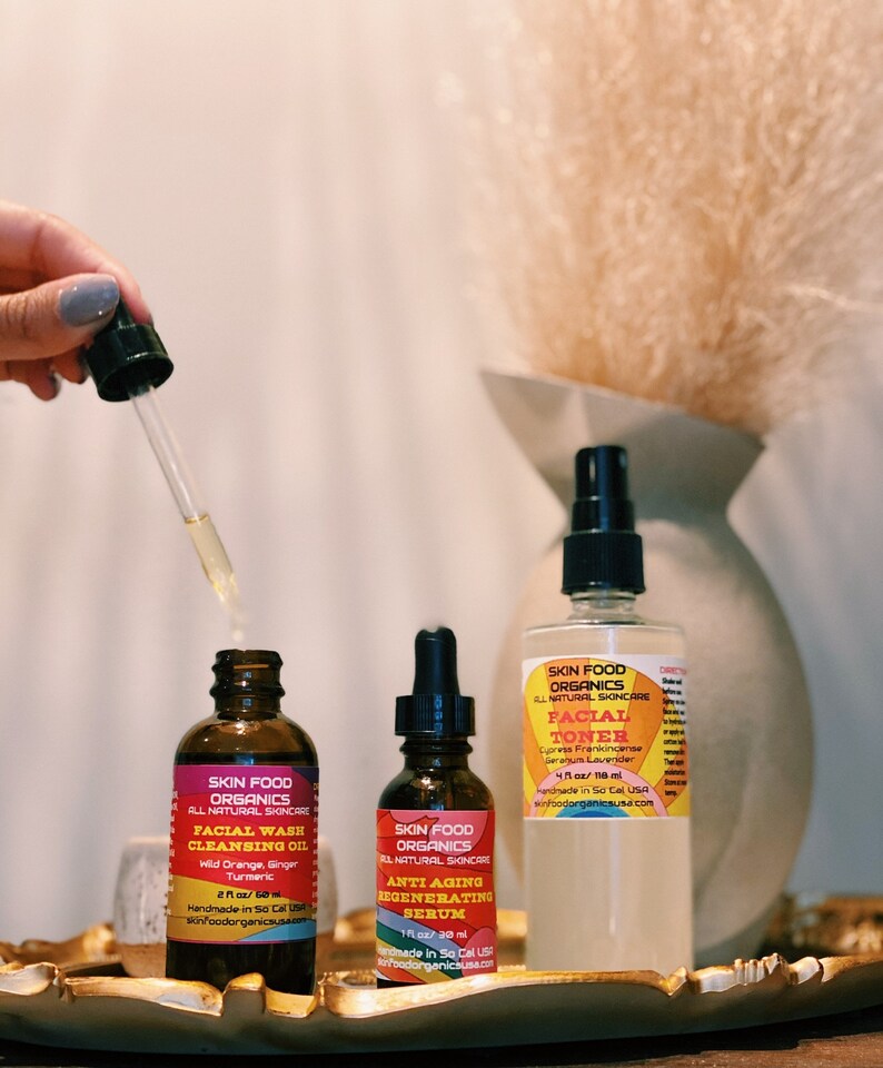 K&ouml;nnte beinhalten: Drei Glasflaschen mit Bio-Hautpflegeprodukten. Die Flaschen sind mit "Skin Food Organics" beschriftet und enthalten Gesichtswasch-Reinigungs&ouml;l, Anti-Aging-Regenerations-Serum und Gesichtswasser. Die Flaschen stehen auf einem goldenen Tablett.