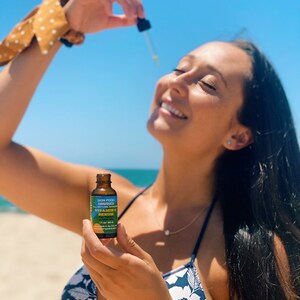 K&ouml;nnte beinhalten: Eine Frau h&auml;lt eine Flasche Skin Food Organics Vitamin C Serum. Die Flasche ist blau und gelb mit wei&szlig;em Text. Die Frau tr&auml;gt ein schwarz-wei&szlig;es Blumen-Bikini-Oberteil und eine goldene Halskette.