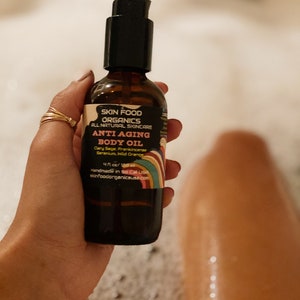 K&ouml;nnte beinhalten: Eine braune Glasflasche mit schwarzer Pumpenaufsatz und einem Regenbogen-Etikett. Das Etikett lautet "Skin Food Organics All Natural Skincare Anti Aging Body Oil Clary Sage, Frankincense, Geranium, Wild Orange 4 fl oz/120 ml Handmade in So Cal USA skinfoodorganicsusa.com".