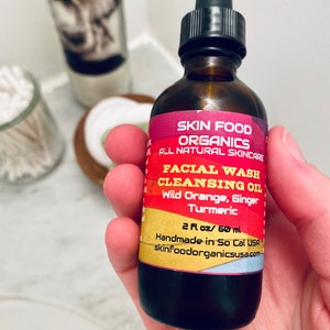 K&ouml;nnte beinhalten: Eine 60 ml braune Glasflasche mit Gesichtswasch-Reinigungs&ouml;l und schwarzem Tropfer. Das Etikett ist rot und gelb mit dem Text "Skin Food Organics All Natural Skincare Facial Wash Cleansing Oil Wild Orange, Ginger Turmeric 2 fl oz / 60 ml Handmade in So Cal USA skinFoodorganicsusa.com".