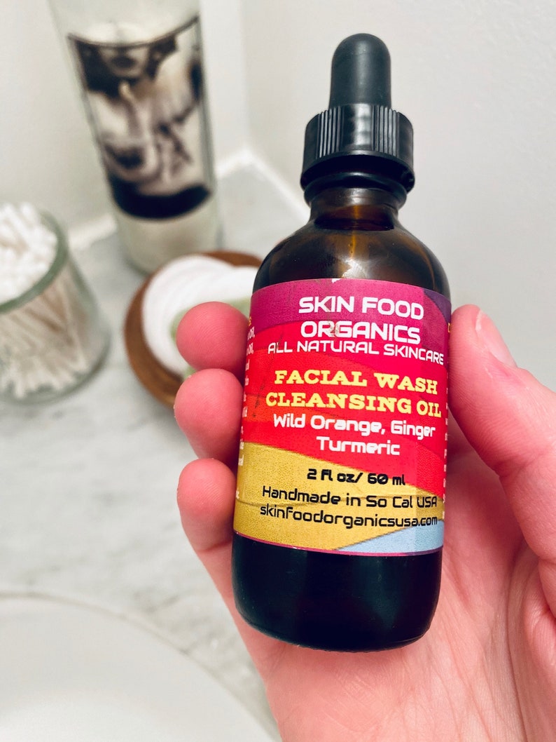 K&ouml;nnte beinhalten: Eine 60 ml braune Glasflasche mit Gesichtswasch-Reinigungs&ouml;l und schwarzem Tropfer. Das Etikett ist rot und gelb mit dem Text "Skin Food Organics All Natural Skincare Facial Wash Cleansing Oil Wild Orange, Ginger Turmeric 2 fl oz / 60 ml Handmade in So Cal USA skinFoodorganicsusa.com".