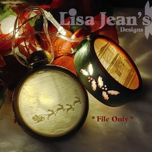 May include: Two illuminated Christmas ornaments, one with a green and white holly design and the other with a white silhouette of a sleigh pulled by reindeer. The ornaments are surrounded by Christmas lights and greenery. The text "Lisa Jean's Designs" and "File Only" are visible in the image.