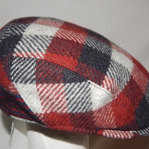 May include: A red, white and black plaid newsboy cap. The cap has a slightly curved brim and a pointed crown.