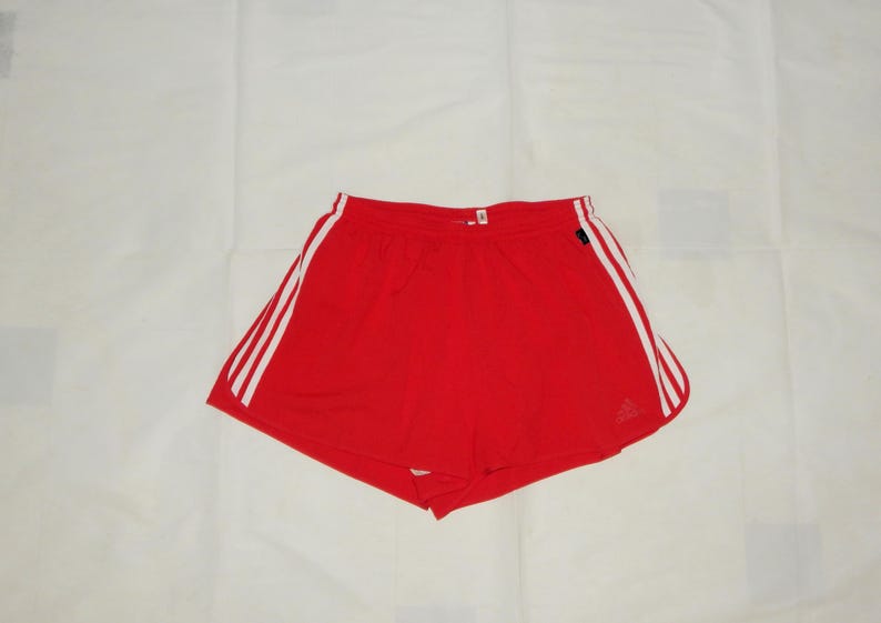 May include: Red athletic shorts with white stripes down the sides. The shorts have a drawstring waist and a small logo on the left leg.