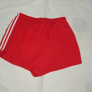 May include: Red athletic shorts with white stripes down the sides. The shorts have an elastic waistband.