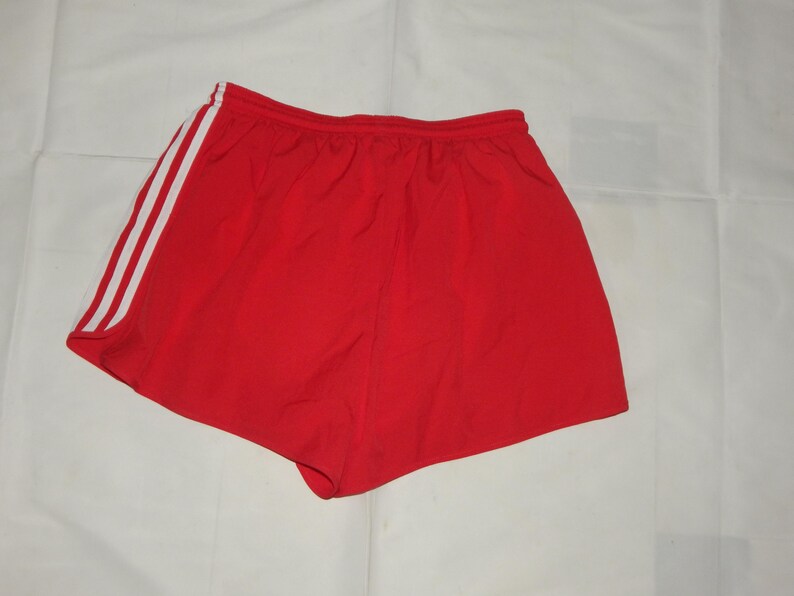 May include: Red athletic shorts with white stripes down the sides. The shorts have an elastic waistband.