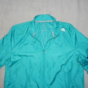 May include: A turquoise blue lightweight jacket with a zipper closure and black and white stripes on the sleeves. The jacket has the Adidas logo on the right chest.