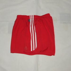 May include: Red athletic shorts with white stripes down the sides and a small Adidas logo on the left leg.