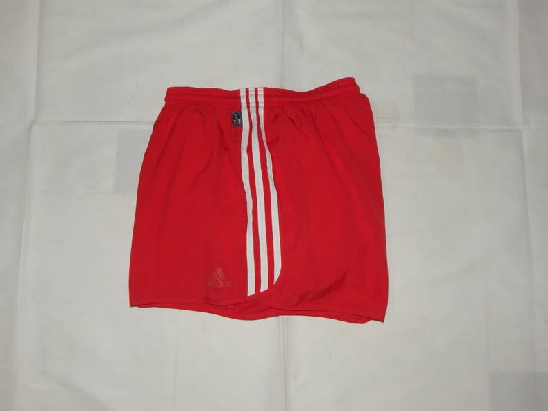 May include: Red athletic shorts with white stripes down the sides and a small Adidas logo on the left leg.