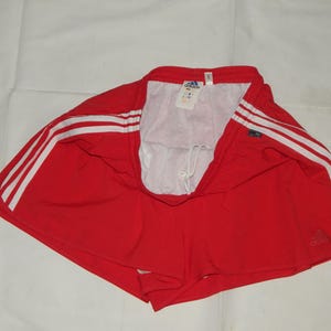 May include: Red athletic shorts with white stripes and the Adidas logo. The shorts have a drawstring waist.