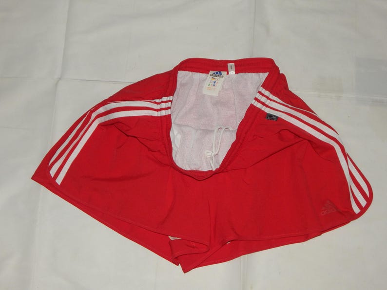 May include: Red athletic shorts with white stripes and the Adidas logo. The shorts have a drawstring waist.